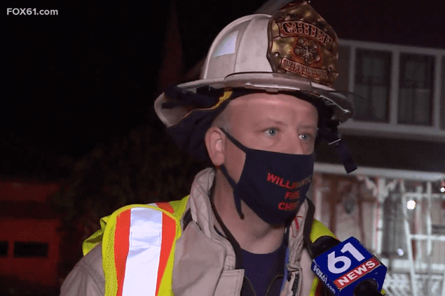 man wearing fire helmet and face mask standing in front of camera speaking